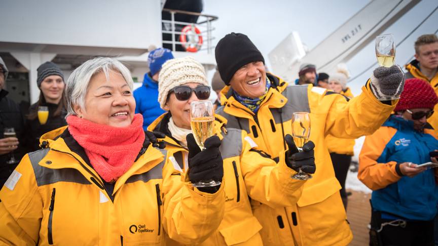 Guests celebrate crossing the Antarctic Circle with sparkling beverages and taking photos on the deck of the ship.