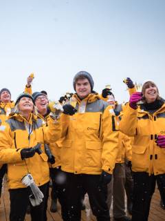 A group of guests (about eleven individuals) raise their glasses together for a toast on the outer decks