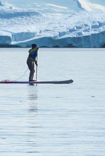 Three guests on their standup paddleboards paddle through calm waters in Antarctica.