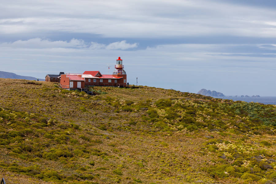 A red lighthouse sits on top of a grassy hill at Cape Horn.