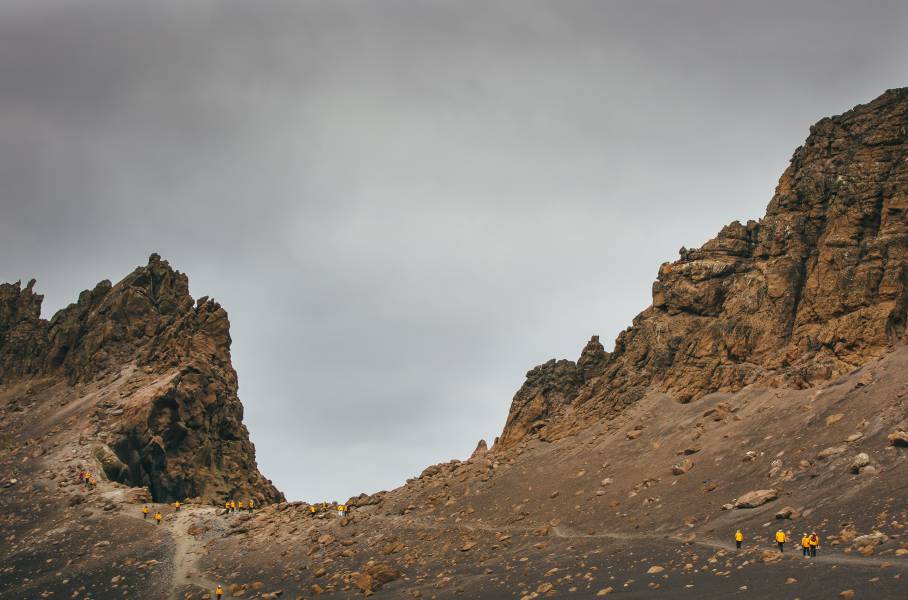 Guests in yellow parkas follow other guests up a hill at Deception Island, Antarctica.