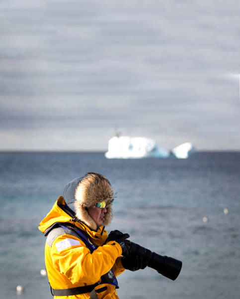 A guest in a yellow parka uses their telephoto lens during a landing in the Antarctic Peninsula.