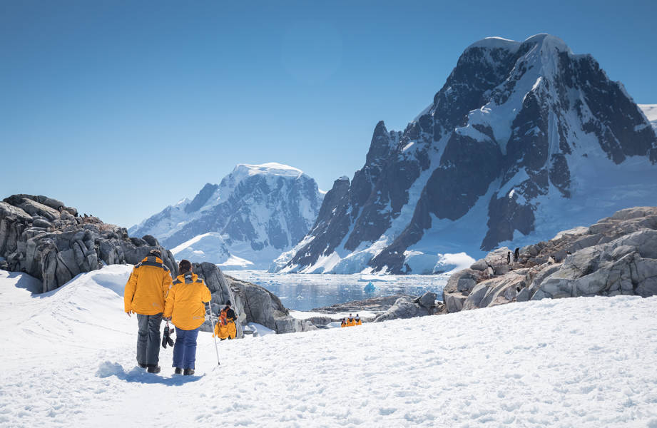 Guests in yellow parkas follow the marked trail at Petermann Island during a sunny day in the Antarctic Peninsula.