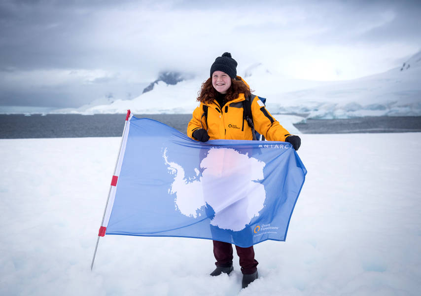 A guest poses with our Antarctic flag with the snowy peaks in the background