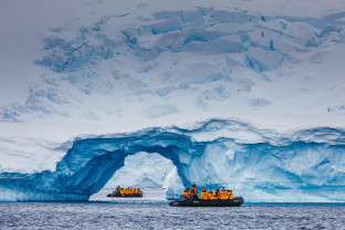 A zodiac boat is spotted through the arch of an iceberg near Cuverville Island. The zodiac boat appears to be close to the iceberg as a result of telephoto lens compression.