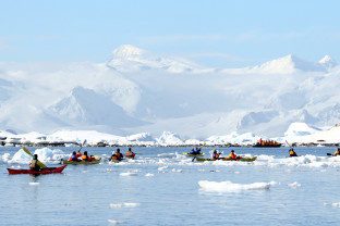 Guests kayaking through frigid waters in Antarctica. Two guides accompany the main group.