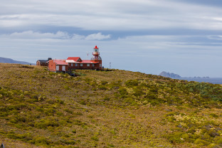 A red lighthouse sits on top of a grassy hill at Cape Horn.