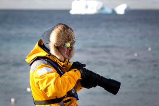 A guest in a yellow parka uses their telephoto lens during a landing in the Antarctic Peninsula.