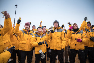 A group of guests (about eleven individuals) raise their glasses together for a toast on the outer decks