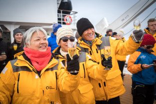 Guests celebrate crossing the Antarctic Circle with sparkling beverages and taking photos on the deck of the ship.