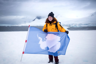 A guest poses with our Antarctic flag with the snowy peaks in the background