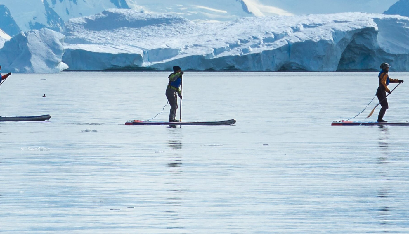Three guests on their standup paddleboards paddle through calm waters in Antarctica.